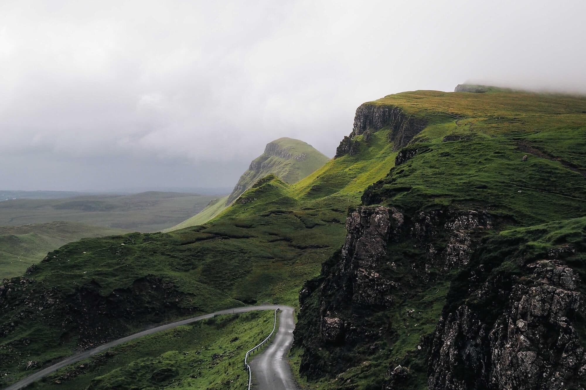 A winding road through green Highland ridges under low cloud