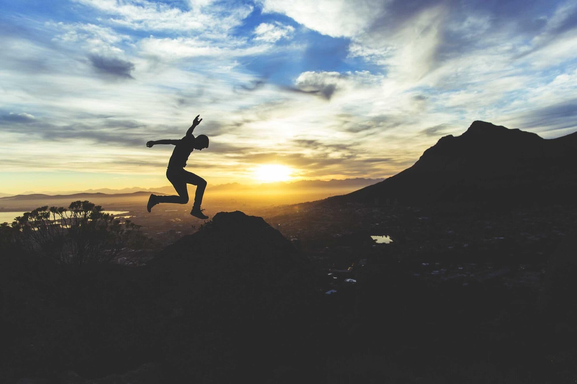 A person leaping between rocks on a hilltop as the sun sets behind them